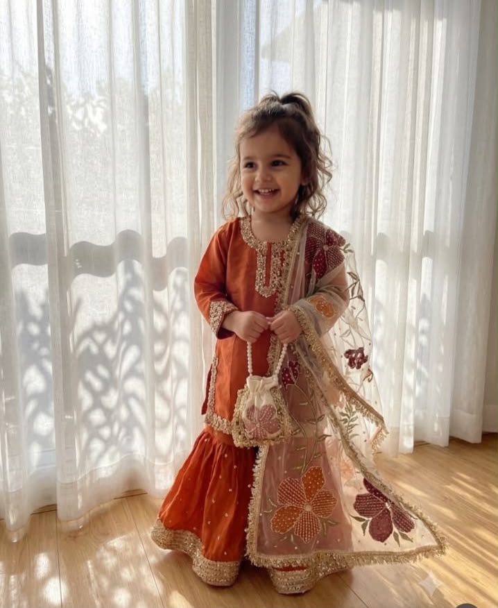 Girl wearing a burnt orange hand-painted garara set with a lace-trimmed shirt and floral organza dupatta
